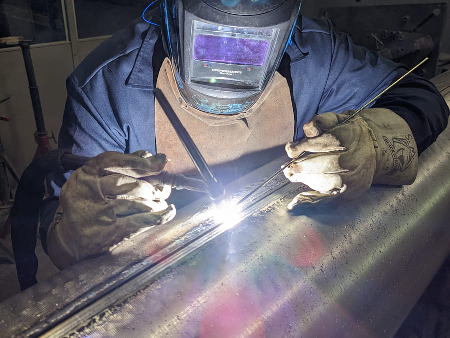Welder applying a TIG weld overlay to a large industrial roll at HFW Industries